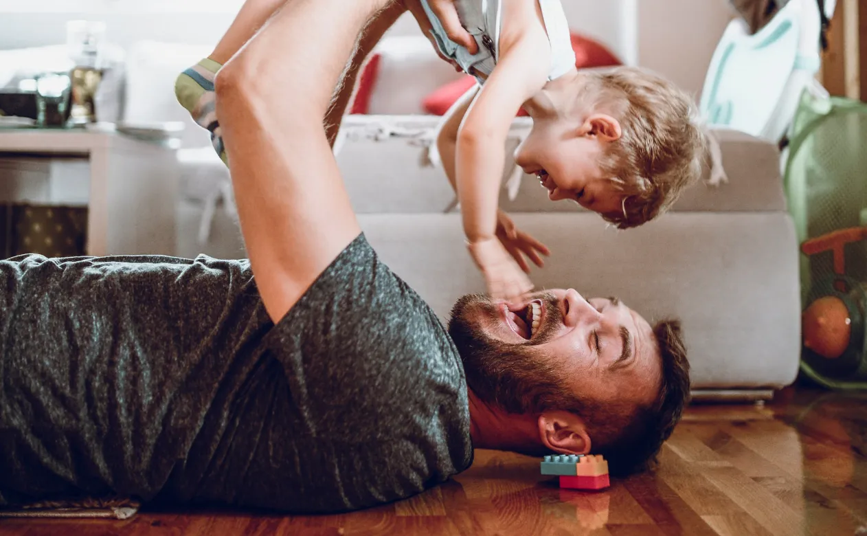 Dad laying on his hardwood flooring holding his son up in the air as they play