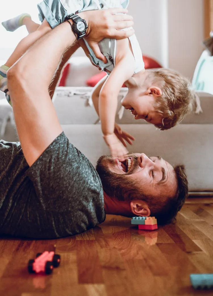 Dad laying on his hardwood flooring holding his son up in the air as they play